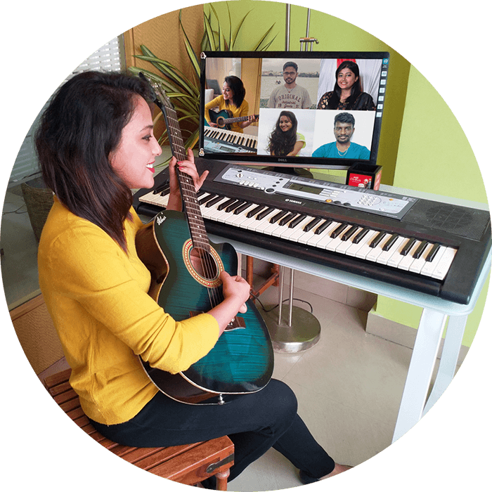 Woman playing a guitar with music keyboard in front and a monitor showing the audience watching her virtual performance